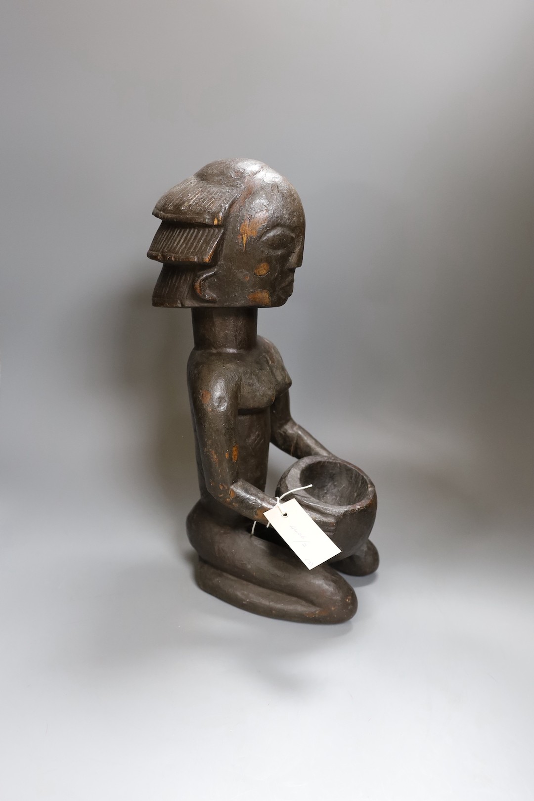 An African tribal carved wood kneeling figure holding bowl (44cm high) and tribal hand instrument (2)